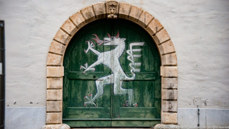White Styrian panther painted on a dark green arched wooden door framed by rusticated stone blocks.