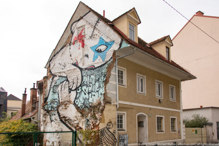 Large colorful graffiti mural covering the exposed gable wall of a small house in Graz.