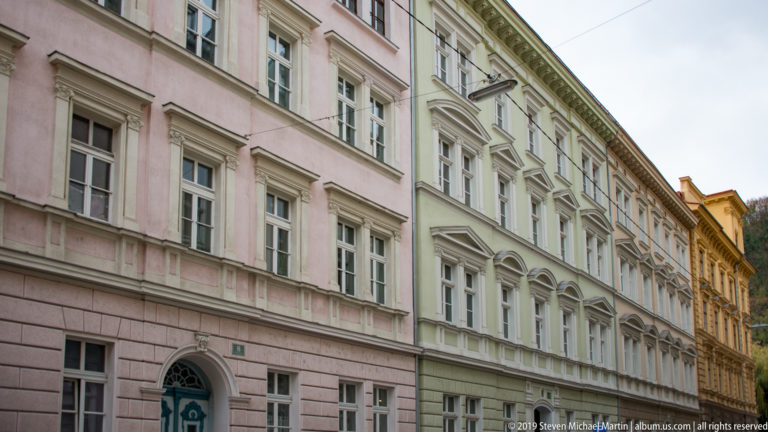 Row of pale pink, green, and cream historic facades with tall windows and classical detailing along a Graz street.