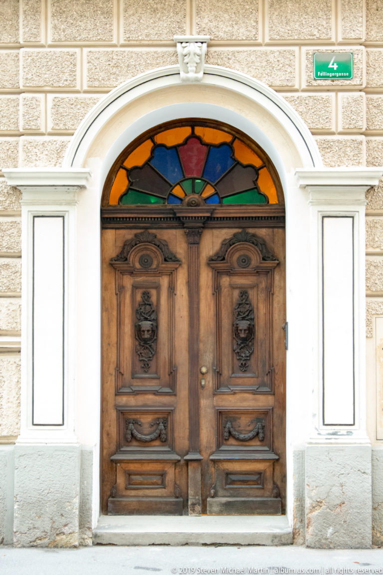 Carved double wooden entrance door beneath a semicircular multicolored stained-glass fanlight in a rusticated facade.