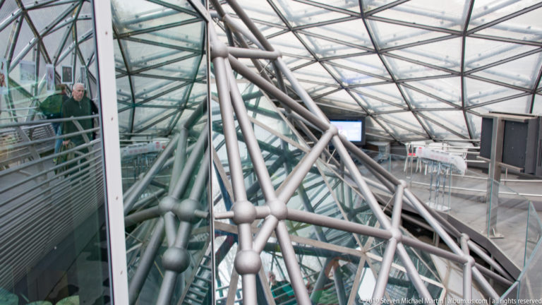 Close view of Murinsel tubular steel members, spherical joints and glazed roof with reflections and seating beyond.
