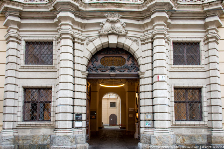 Symmetrical rusticated stone gateway with gridded windows and an aligned interior passage beyond the arch.