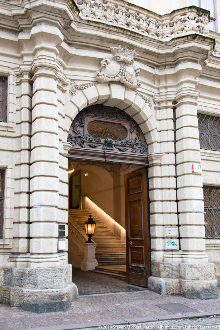 Rusticated stone palace entrance with carved crest, open wooden door and broad stairway rising inside.