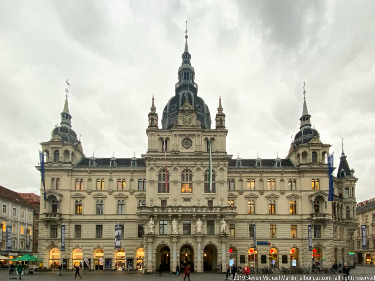 Grand Graz Town Hall façade with central tower and corner pavilions facing Hauptplatz under a cloudy sky.