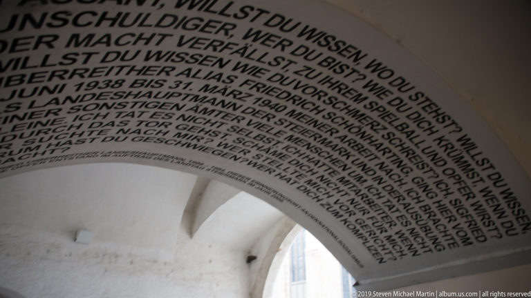 Large black German text painted across the curved white surface of a vaulted archway.