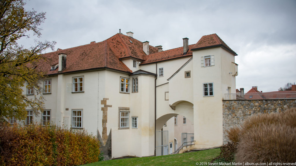 White historic building with red tile roofs and arched gateway opening through the lower story.