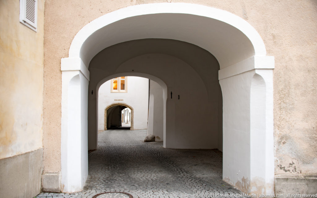 Series of white vaulted archways receding over cobblestone paving through a historic Graz building.