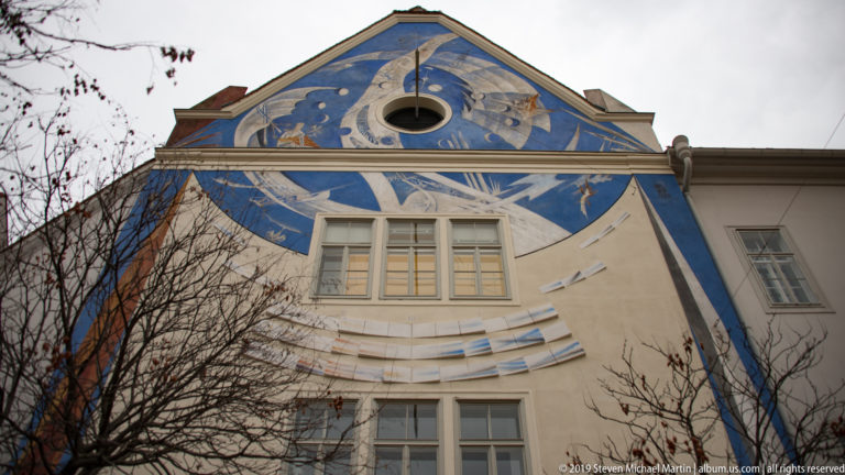 Blue-and-white mural covering a triangular building gable with rectangular windows in Graz.