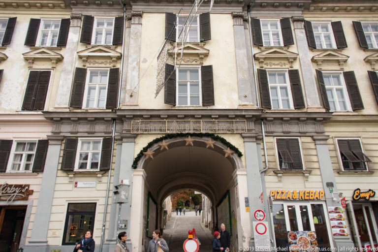 Historic building façade with shuttered windows and large arched passageway opening onto an inner lane.