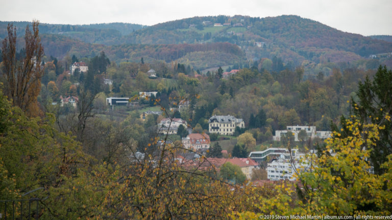 Wooded hillside with scattered houses and autumn trees on the slopes above Graz.