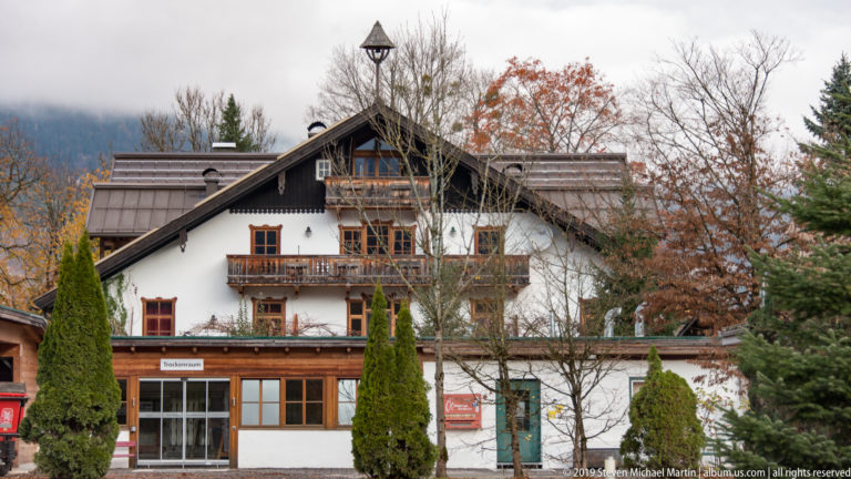 Large white-and-timber chalet-style building with multiple wooden balconies, steep gables, and trees in front.