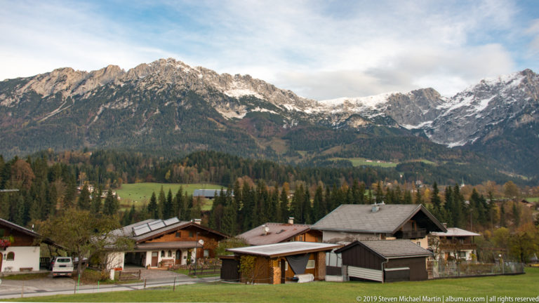 Village houses and farm buildings below a broad rugged mountain ridge with snow in high gullies.