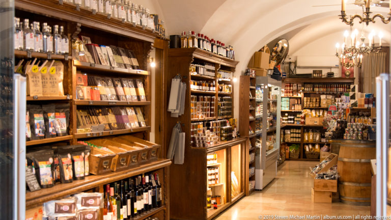 Warmly lit specialty shop with wooden shelves of packaged foods, bottles and jars beneath an arched ceiling.
