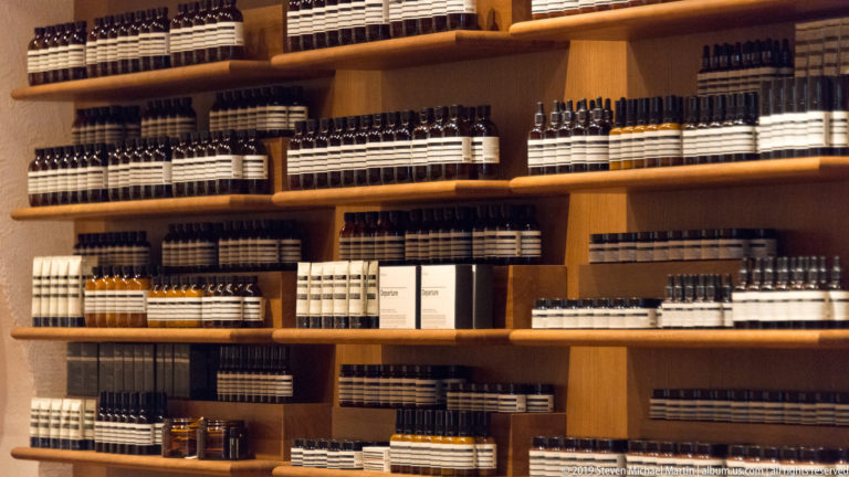 Warm wooden shop interior with shelves densely stocked with rows of small bottles and boxed products.