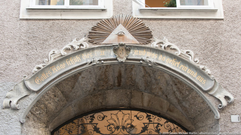 Close detail of a stone passage arch with white scroll ornament, a curved German inscription and a small triangular motif above.