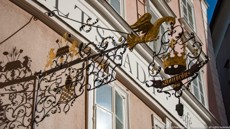 Elaborate black-and-gold wrought-iron shop sign with a crown, gilded figure, scrollwork and the date 1792.