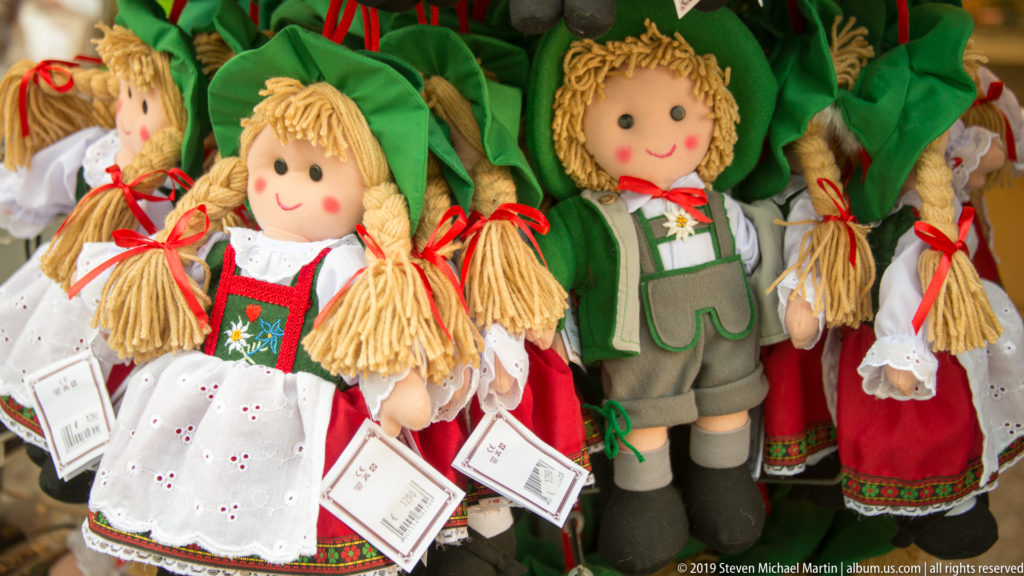 Group of smiling cloth dolls with braided hair, green hats, dirndl-style dresses and lederhosen-style outfits.
