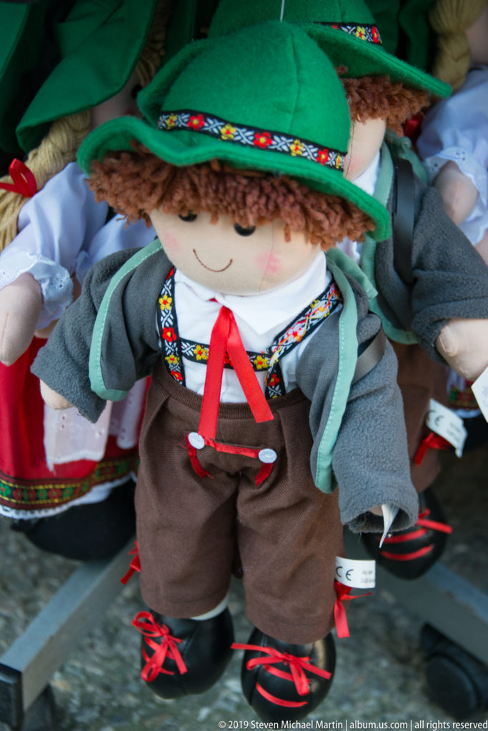 Cloth souvenir doll wearing a green hat, embroidered Alpine-style clothing, brown shorts and red-laced shoes.
