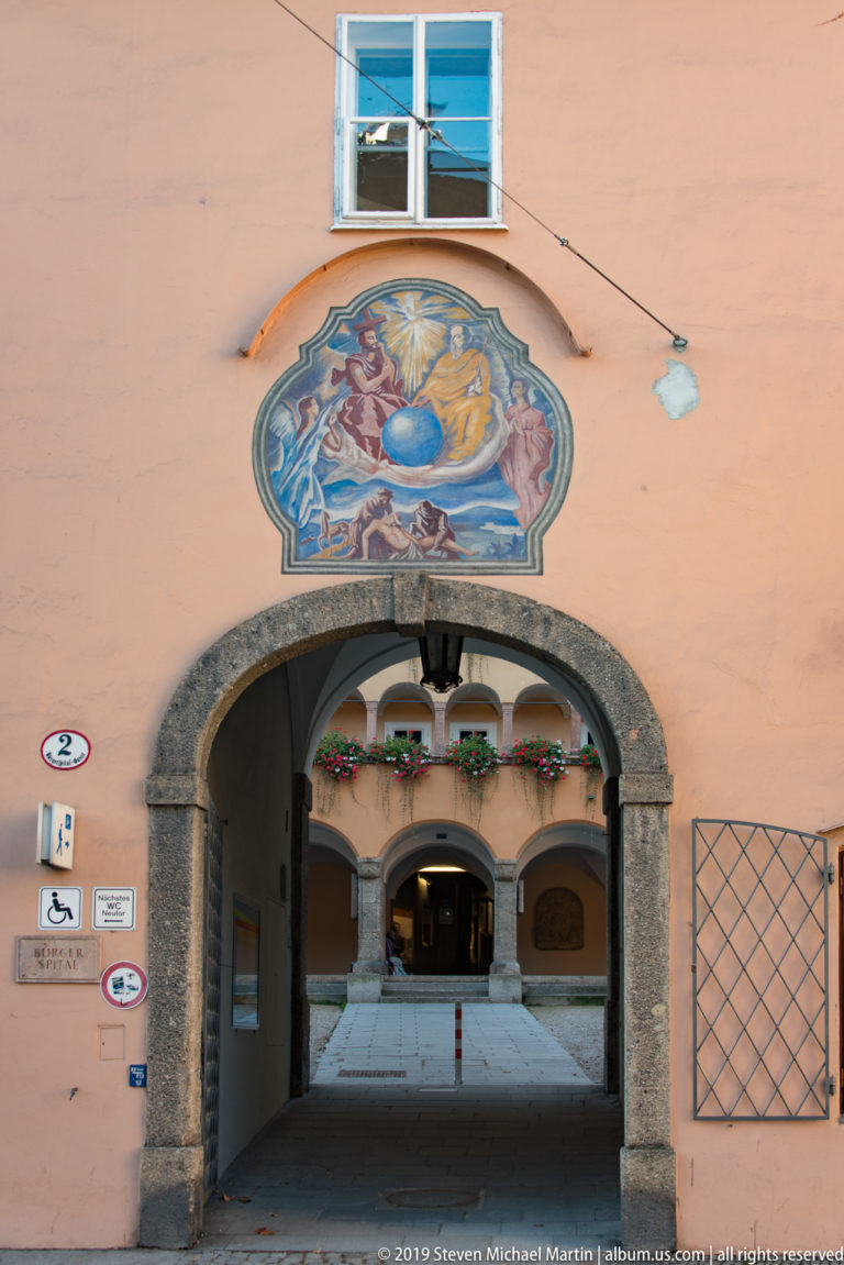 Colorful devotional mural above a broad stone arch, with an open passage leading into a courtyard below.