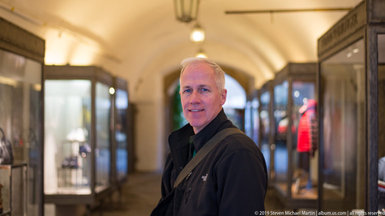 Man standing in a vaulted Salzburg passage lined with lit glass display cases and shops.