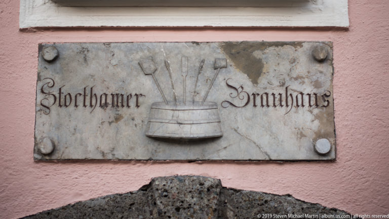 Weathered stone plaque reading Storthamer Salzburg with a carved central barrel-like emblem on a pink wall.