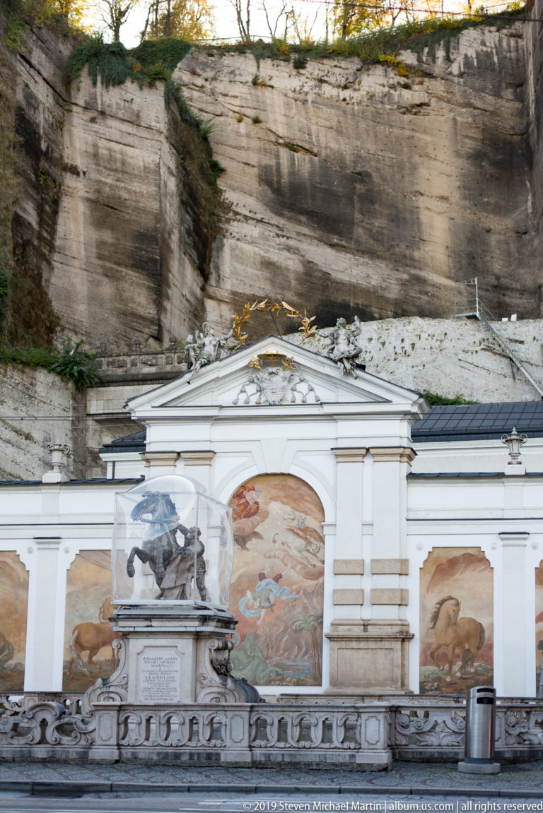 Baroque Pferdeschwemme horse pond with horse sculpture, painted equestrian panels, white wall, and rock face behind.
