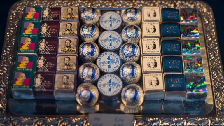 Shop display filled with Mozart-themed chocolates and souvenirs in portrait wrappers, round tins, and boxed rows.