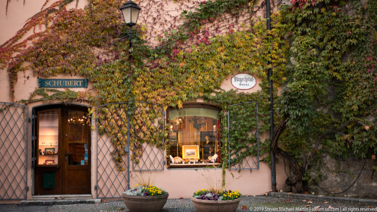 Ivy-covered pink shopfront with a SCHUBERT sign, lit display window, lantern, trellis, and flower planters.