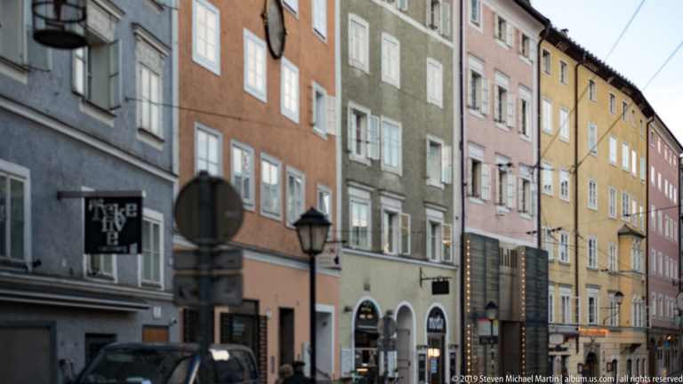 Narrow historic street lined with colorful multistory façades, repeated windows, shop signs, and lamps.