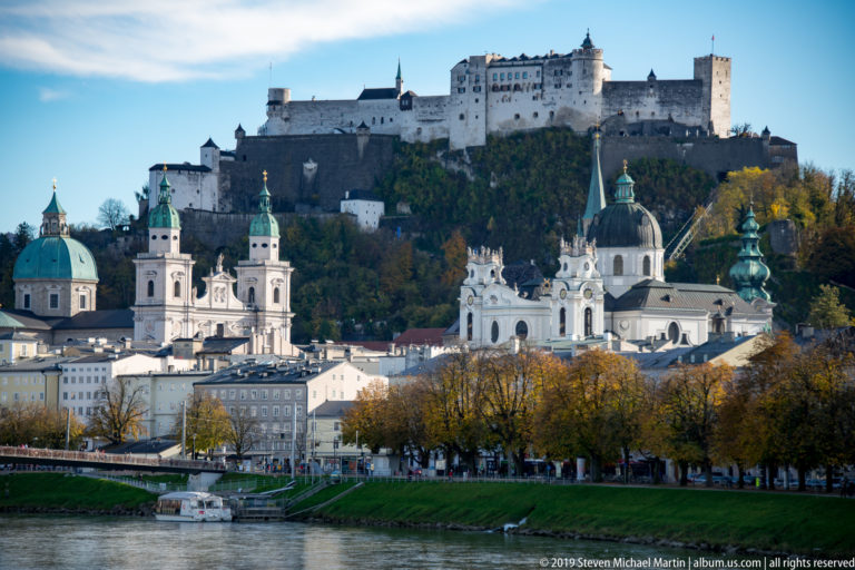 Baroque domes and church towers along the Salzach beneath Hohensalzburg Fortress on its wooded hill.
