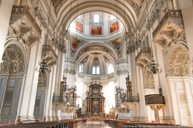 Longitudinal cathedral interior looking toward the high altar, with massive piers, arches, galleries, chandeliers, and domed sanctuary.