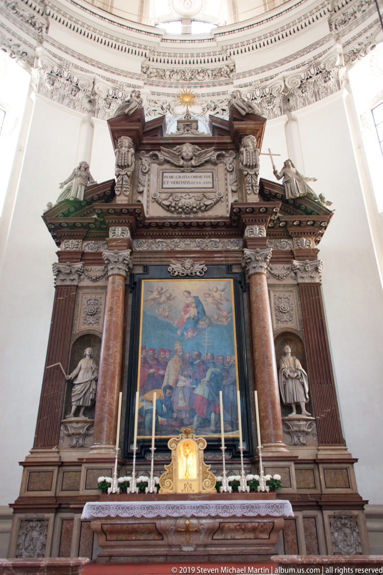 Frontal view of a monumental side altar with painted altarpiece, paired columns, statues, candles, and gilded liturgical furnishing.