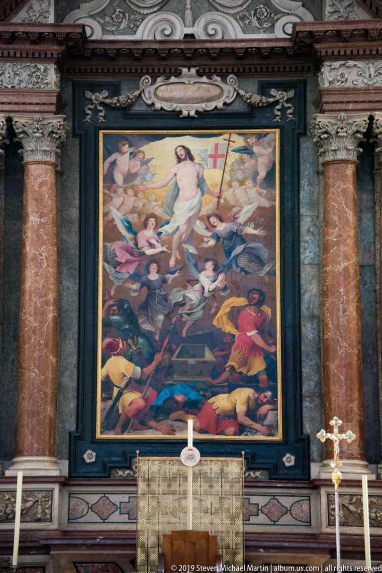 Side altar with Resurrection painting framed by reddish marble columns above an altar table and candlesticks.