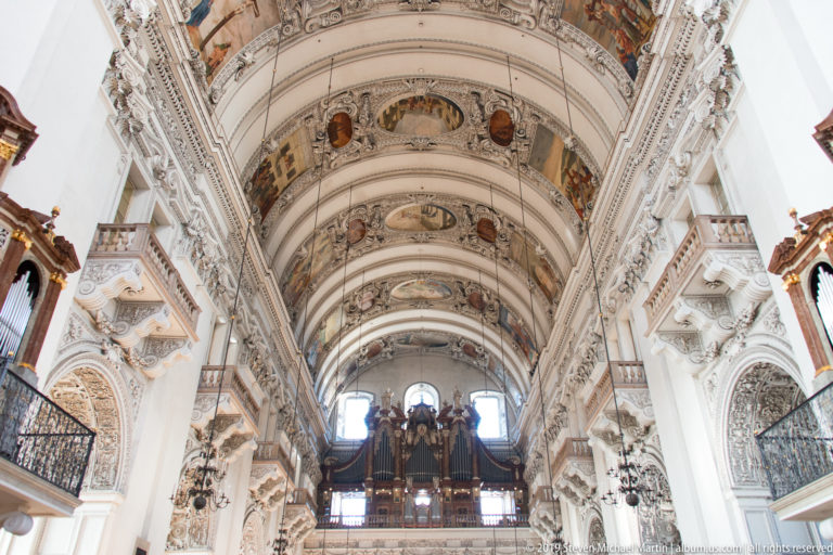 Upward view along painted and stuccoed nave vaults toward a distant pipe organ gallery.