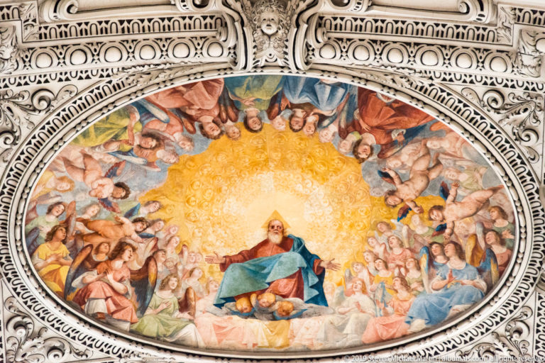 Oval fresco of an enthroned bearded figure amid angels and saints, enclosed by ornate white stucco.