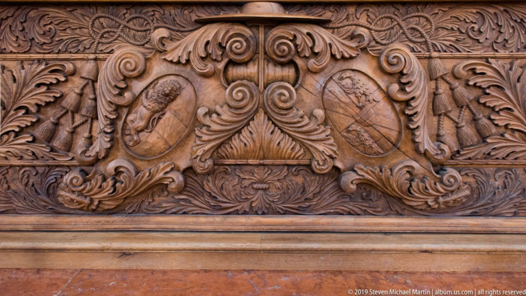 Close view of a carved wooden panel with two oval emblems surrounded by dense foliate scrollwork.