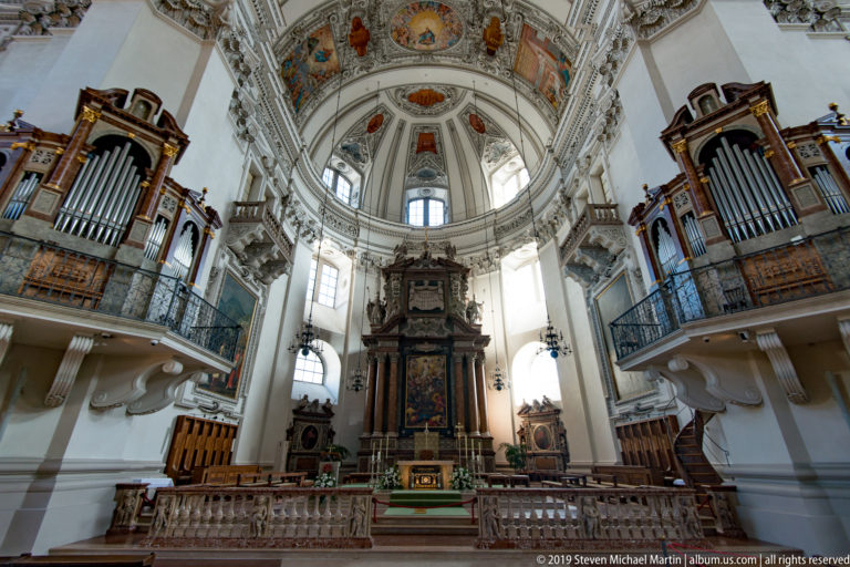 High altar beneath the painted dome, flanked by dark wooden pipe organs on projecting galleries.