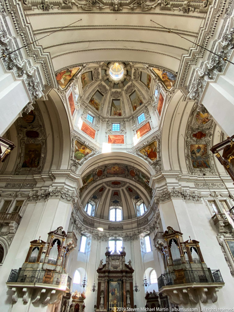 Wide low-angle sanctuary view with high altar, paired organ galleries, arched windows, decorated apse, and crossing dome overhead.