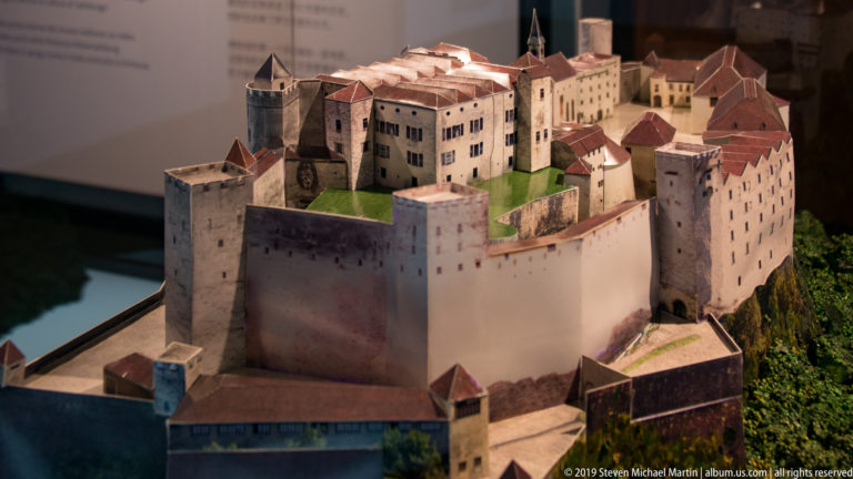 Oblique view of a Fortress Hohensalzburg model with massive outer walls, towers, and clustered red-roofed buildings.