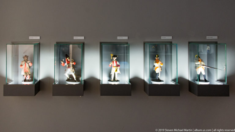 Five historical soldier figures in different uniforms displayed individually in illuminated wall-mounted glass cases.