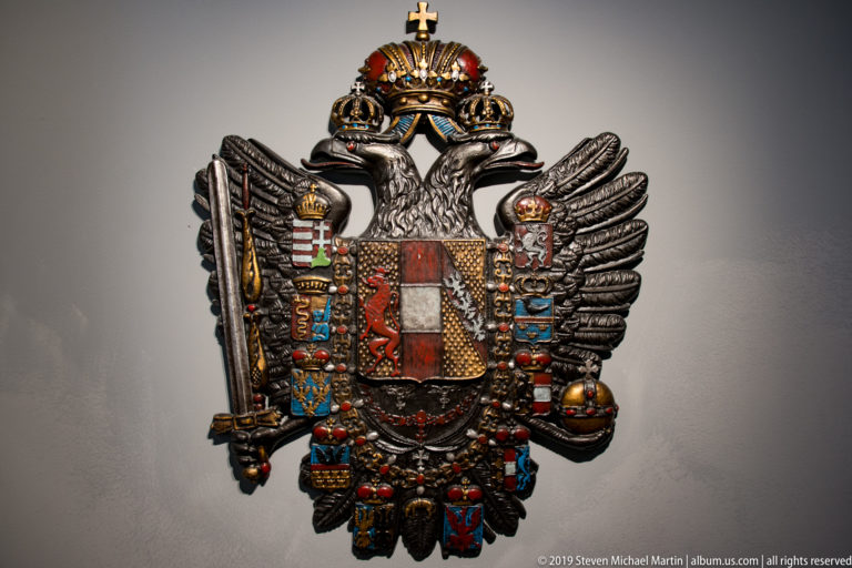 Ornate crowned double-headed eagle bearing a multicolored quartered shield, scepter, orb, and pendant insignia.