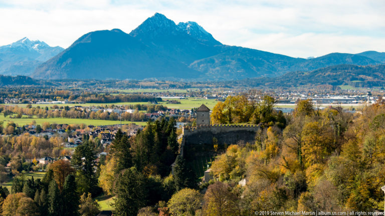 Stone defensive outwork with parapet and small tower among autumn trees, overlooking the Salzburg basin and mountains.