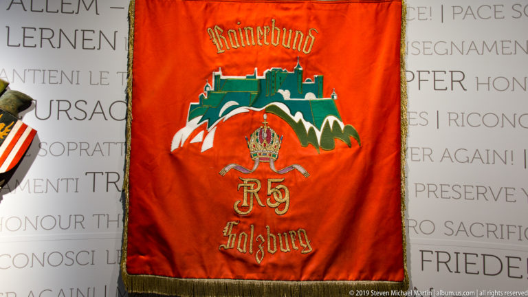 Red Rainerbund Salzburg banner with embroidered fortress emblem, crowned monogram, lettering, and gold fringe.