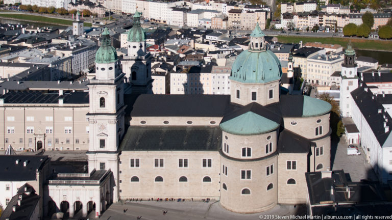 Elevated close view of Salzburg Cathedral with green dome, twin towers, and surrounding historic buildings.