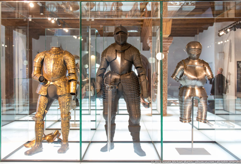 Three suits of metal armor displayed side by side in tall glass cases inside the fortress museum.