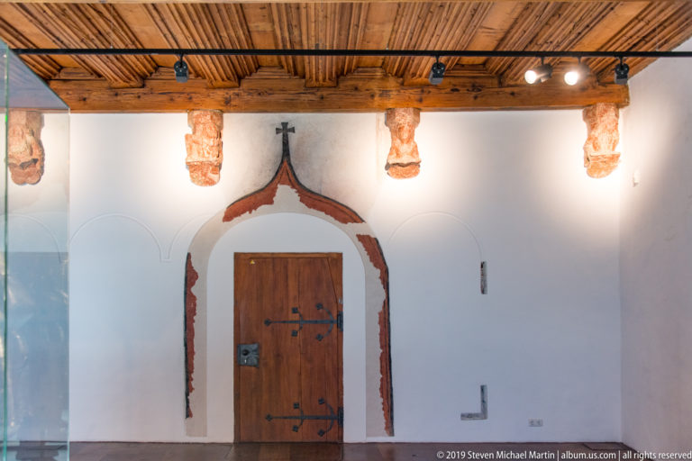 Wooden door in a pointed painted arch below a timber ceiling and a row of carved wall corbels.