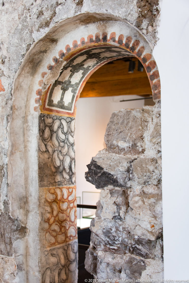Arched doorway with faded painted motifs, exposed brick, and rough stone masonry along the opening.