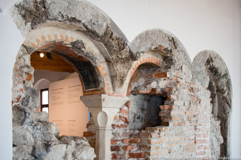 Exposed brick arches, rough stonework, and a small column revealed within a museum interior.