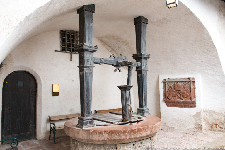 Timber lifting mechanism mounted over a circular stone basin inside a white vaulted fortress room.
