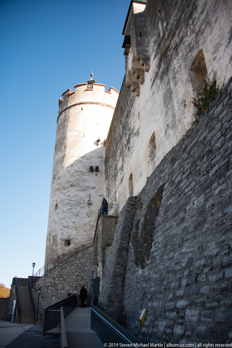 Low-angle view of a round white fortress tower above a thick sloping stone defensive wall.